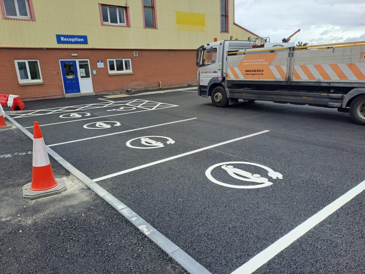 A white car with a plug stencilled onto a car parking space to depict an EV charging spot. 